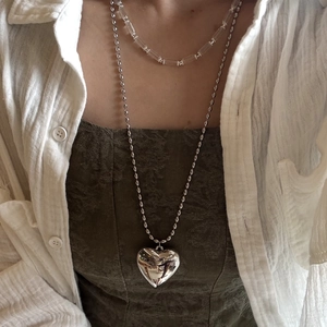 Close-up of a long silver metal heart necklace layered with a clear beaded choker on a model