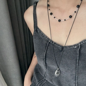 Layered beaded necklace with silver teardrop pendant shown on a denim vest