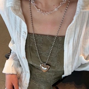 Detail of a large silver heart pendant and layered crystal bead necklace on a model