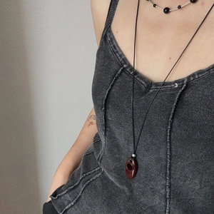 Close-up of a long cord necklace featuring a dark reddish-brown teardrop hollow pendant