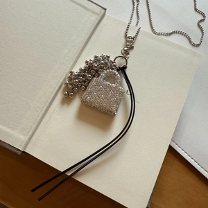 Macro shot of silver bead chain necklace featuring a crystal handbag pendant on a book