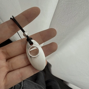 Detailed close-up of matte silver oval pendant with cutout on long black cord necklace
