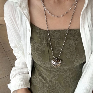 Detail of layered silver beaded necklace with large polished heart pendant on model