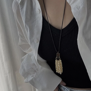 Close-up of a long tassel necklace with gold beads on a minimalist linen shirt