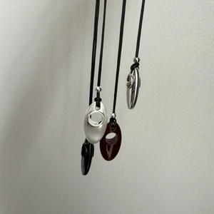 Detail of four geometric oval pendants in silver, amber, and black on minimalist cords