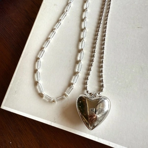 Close-up of a silver-toned metal ball chain necklace with a large polished heart pendant