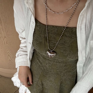 Close-up of layered silver ball chain necklace with large heart pendant on a model
