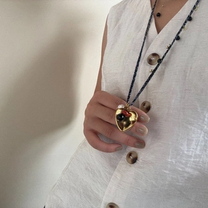 Detail of a large gold heart pendant with colorful beads on a woven tassel necklace