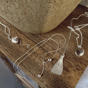 Three silver brushed heart pendants and tassel long sweater necklaces on wood