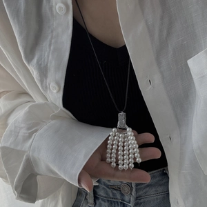 Detailed view of pearl tassel pendant with silver metal connector on black cord necklace