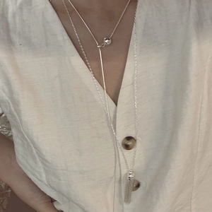Silver layered tassel necklace with heart pendant and slider beads on a linen shirt
