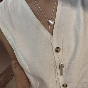 Detail of layered silver necklaces with heart pendant and tassel on silk clothing