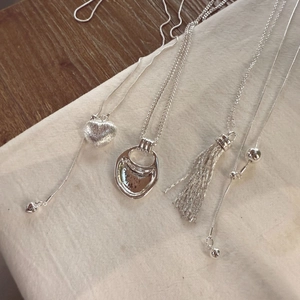 Detail of four silver heart and tassel pendants on textured fabric and wood background