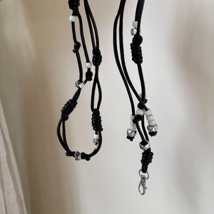 Detail of black woven cord with white beads and silver geometric charms for fashion accessories