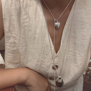 Detail of layered silver heart pendant and hollow horseshoe necklace on linen shirt