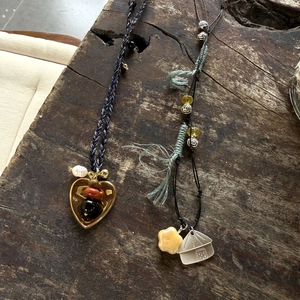 Handmade woven necklace with heart and star charms on a rustic dark wood background