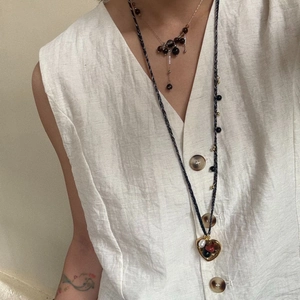 Detail of layered gold snake chain and tiger eye stone necklace on a beige linen shirt