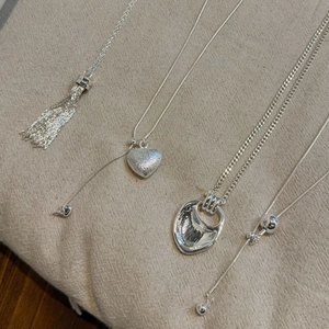 Detail of four silver pendant necklaces featuring heart, tassel, and bead designs