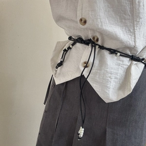 Minimalist black braided waist chain with silver charms and tassels on a linen shirt