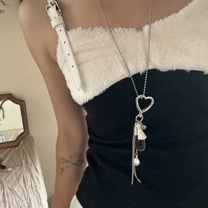 Detail view of heart pendant long necklace with water drop charm and white tassel on model
