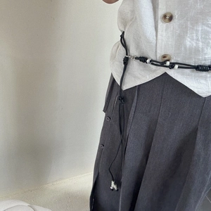 Detail of a black woven waist chain with beads on a linen shirt and pleated skirt