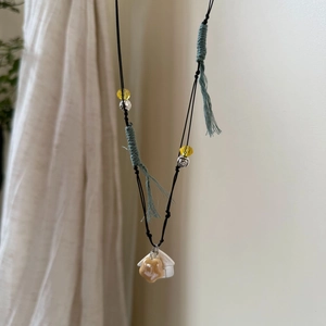 Detail of hand-woven rope necklace with ceramic star and house charms plus green tassels