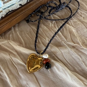 Detail of a gold heart pendant with baroque pearl and woven rope on textured fabric
