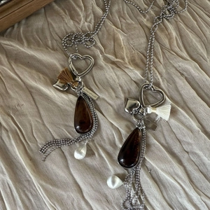 Detailed close-up of brown teardrop pendant with heart clasp and tassel on fabric