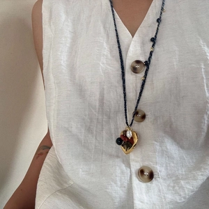 Detail of hand-woven long necklace with golden heart pendant and natural stone on white vest