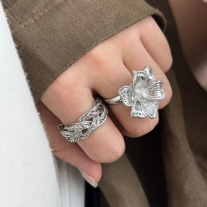 Détail d'une bague fleurie en argent brossé et d'un large anneau tressé sur le doigt