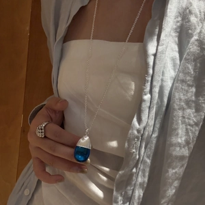 Detail einer langen silbernen Kette mit einem durchscheinenden dunkelblauen Tropfenanhänger