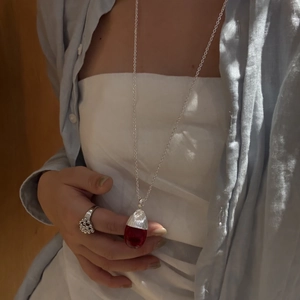 Detail einer langen silbernen Kette mit einem klaren roten Tropfen-Kristall-Zapfen-Anhänger