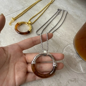 Detail shot of amber tortoise shell resin and metal ring pendant on a beaded chain
