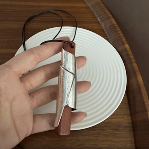 Dettaglio del ciondolo minimalista in legno con metallo argentato martellato su cordino