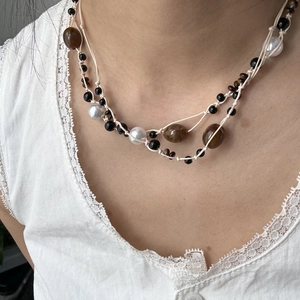 Detalle de collar bohemio de varias capas con perlas blancas y cuentas marrones en encaje