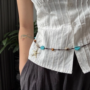 Detalle de cadena de cintura boho con cuentas turquesas, conchas y colgante de estrella