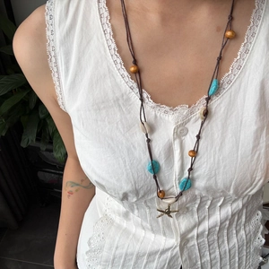 Detalle de un collar hecho a mano con turquesa, concha y colgante de estrella de mar dorada