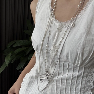 Macro detail of layered pearl necklace with silver dachshund dog pendant on lace background