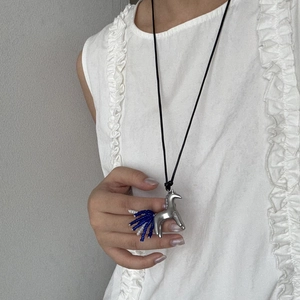 Dettaglio del ciondolo a unicorno con perline bianche e blu su una collana lunga nera