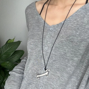 Silver dachshund pendant necklace with black cord shown on a model wearing grey knitwear
