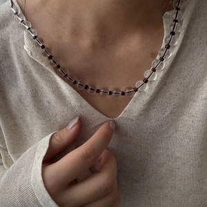 Detail der Perlenkette mit transparenten Kristallen und dunkelroten Akzenten am Hals