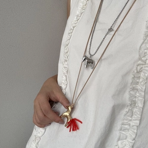 Dettaglio di una collana lunga con pendente a cavallo e nappa rossa su modella