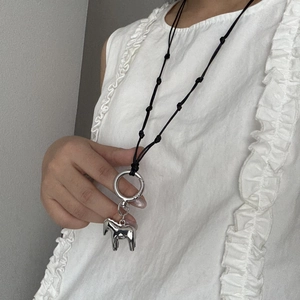 Dettaglio del ciondolo pony argento su collana lunga con perline su top bianco