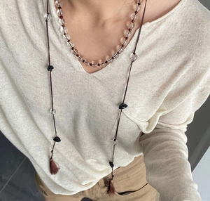 Detail einer mehrlagigen Boho-Perlenkette mit brauner Quaste auf Strickoberteil