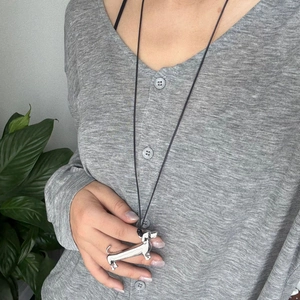 Close-up of a silver dachshund pendant on a minimalist black cord worn by a model
