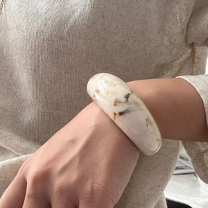 Close-up of wide cream resin bracelet with brown marble texture worn on knit sleeve