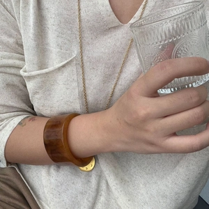 Close-up of a wide amber resin bangle with tortoiseshell texture worn by a model
