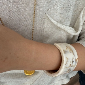 Close-up of wide resin bangle with brown marble texture worn with beige knitwear