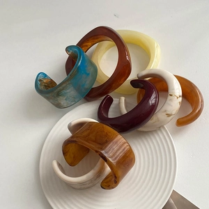 Close-up of colorful marbled resin bangles and C-shaped cuffs on a ceramic tray
