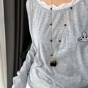 Detailaufnahme einer langen Goldkette mit schwarzen Perlen und Mini-Taschenanhänger